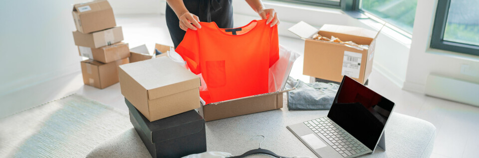 kvinne tar ut en t-skjorte fra en pappeske blant flere pappeske-stabler og en laptop