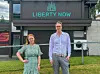 Camilla Moen og Einar Uvsløkk foran brunt bygg med Liberty Now-logo.
