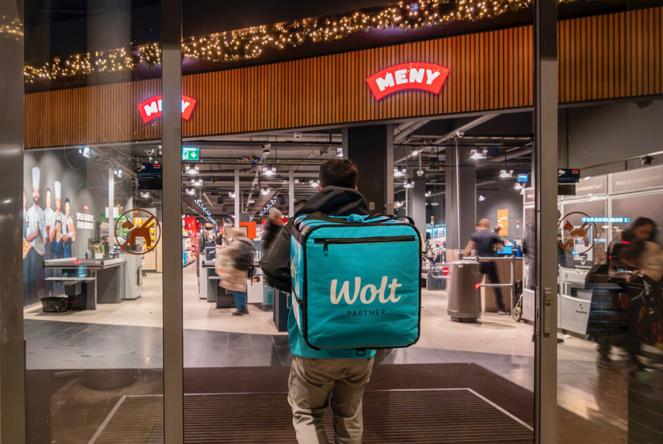Nå kan kunder i Oslo og deler av Bærum få et bredt utvalg av dagligvarer levert på døren når Wolt og MENY samarbeider. Wolt-bud foran en Menybutikk