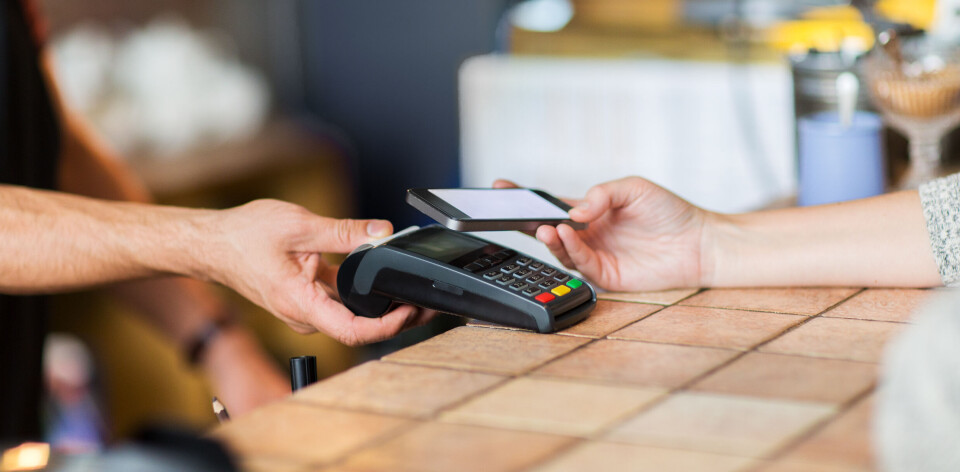 Nets har gjennomført en kampanje hvor de oppfordret sine partnere til å bli med på å resirkulere POS-terminaler på en bærekraftig måte. modern technology and people concept - man or bartender with payment terminal and customer with smartphone at bar of coffee shop