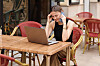 kvinne på uteservering i telefon med laptop