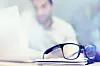 Blur, notebook and glasses on desk with man in office for planning, schedule and agenda on table. Laptop, eyewear or worker copywriting with diary journal for business, administration or email on web.