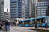Blå trikk og fotgjengere ved Jernbanetorget i Oslo, omgitt av høye kontorbygg.