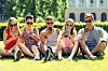 friendship, leisure, summer, technology and people concept - group of smiling friends with smartphones sitting on grass in park.