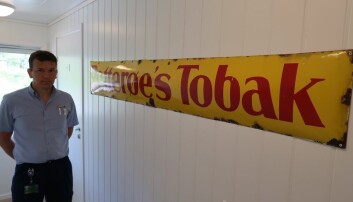 Idar Larsen med Petterøes Tobak-skiltet som illustrerer butikkens historikk.