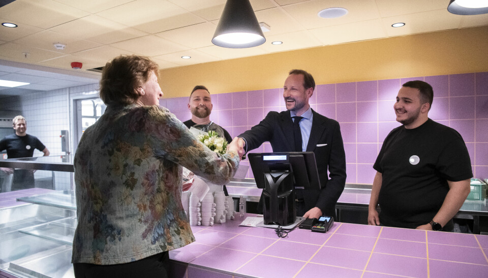 Kronprins Haakon og Oslo-ordfører Marianne Borgen på hver sin side av en rosa disk. Hilser på hverandre, Kronprisen står ved kasseapparatet.