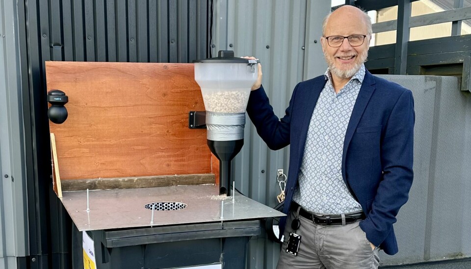 Dag Einar Solberg viser DeBoss-avfallsbeholderen med fôringsautomaten på brettet. Fuglene skal læres opp til å slippe søppelet i åpningen til beholderen.